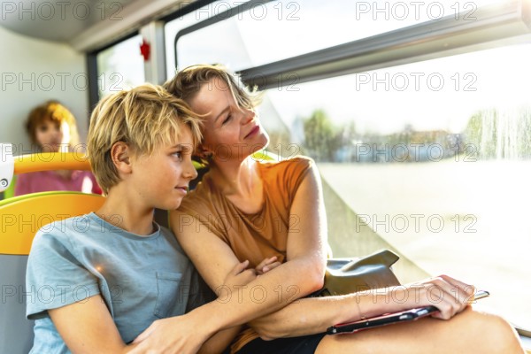 Mother and son relaxing and enjoying the warm sunlight streaming through the window while traveling by public bus, representing family connection, urban commute, and modern lifestyle