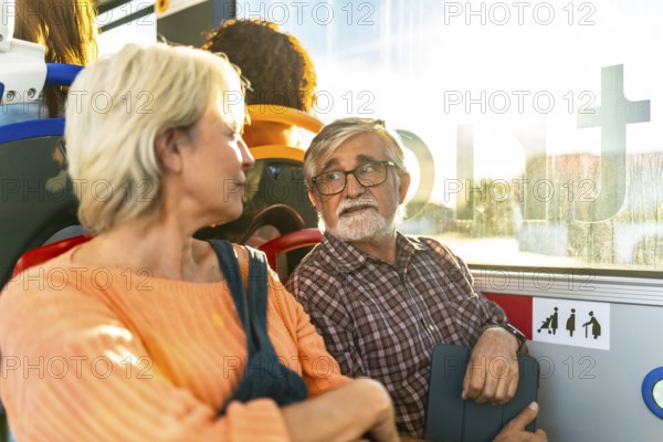 Senior couple sitting on a city bus, chatting and smiling as sunlight streams through the window with warm lens flare, relaxed and enjoying their journey together