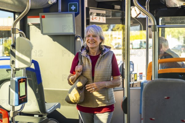 Senior woman standing, holding a bag, and smiling while traveling on a modern public transit bus, enjoying her journey and using sustainable transportation
