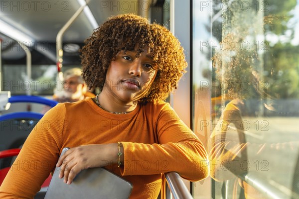Young black woman with curly hair traveling on public transport, catching golden hour daylight during her daily commute, creating a thoughtful and relaxed atmosphere