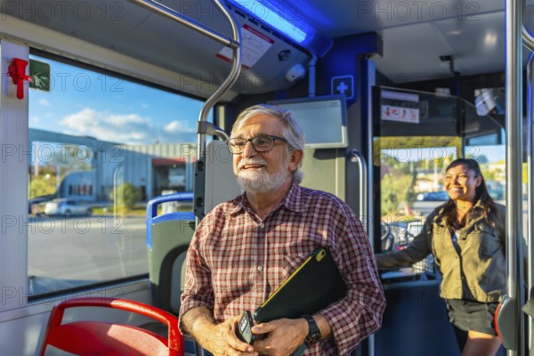 Senior male passenger holding a digital tablet and phone, smiling and looking out the window while traveling on a modern public transport bus enjoying the journey
