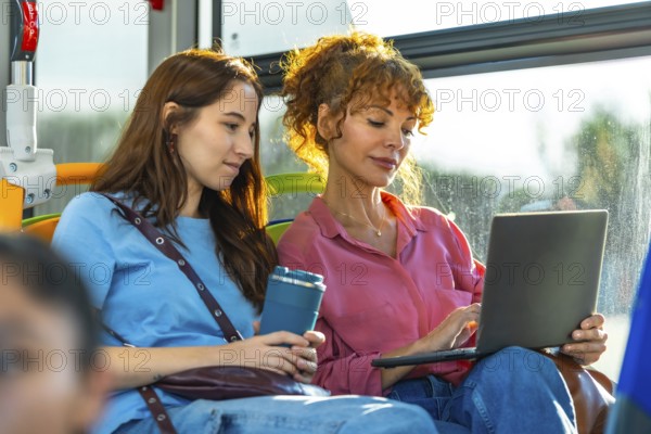 Two women traveling on public transport, one working on a laptop, demonstrating remote work flexibility and convenience of using technology during daily commute time