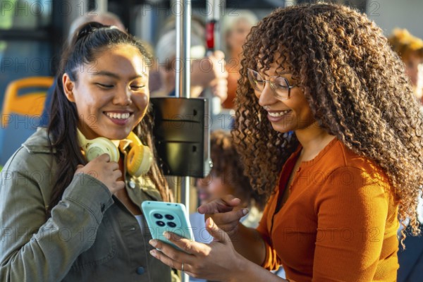 Two smiling multiethnic women bonding and sharing content on a smartphone while commuting together on a public transport bus, enjoying a pleasant journey