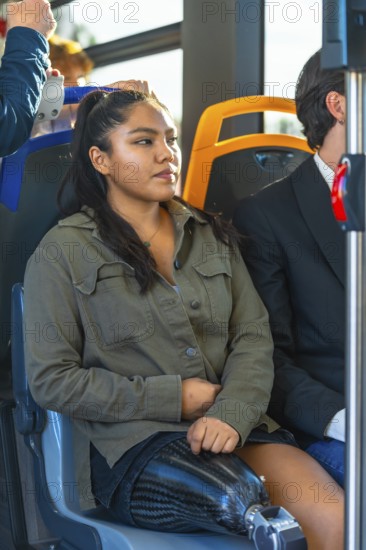 Young woman with a carbon fiber prosthetic leg sitting on public transport, riding a modern bus, showing disability inclusion and independent living through accessible urban mobility
