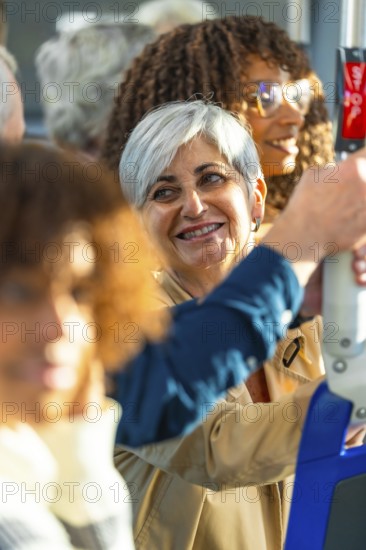 Mature woman with gray hair smiling on a city bus, holding a handrail amid diverse passengers, candid side view capturing everyday urban commute, community and joyful travel moments