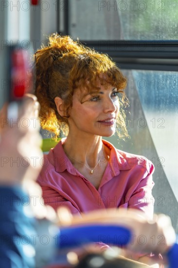 Redhead woman on a city bus, bathed in warm sunlight as she gazes out the window, relaxed and thoughtful during her daily commute through urban streets