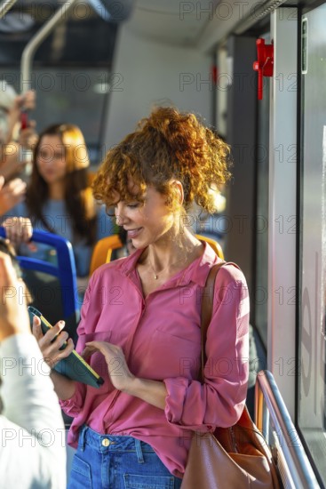 Young woman with red curly hair traveling by bus and checking her smartphone, connecting, communicating, and interacting with her cell phone during daily commute