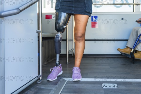 Amputee woman with a prosthetic leg and sneakers standing inside a bus, sharing the accessible public transport space with a person in a wheelchair, representing inclusion and equality