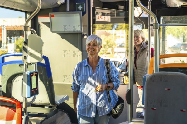 Smiling senior woman standing in a modern public transport bus, enjoying her journey and commuting using accessible urban transportation, with another passenger in the background
