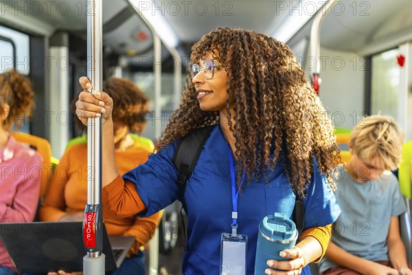 Healthcare professional with curly hair standing in a public transport bus, wearing scrubs while holding a reusable water bottle and her id badge, a symbol of dedication and community service
