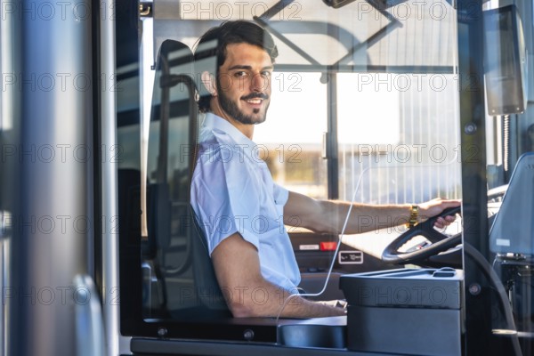Young man working as a bus driver, smiling at the viewer while steering the public transport vehicle, representing professional occupation and service