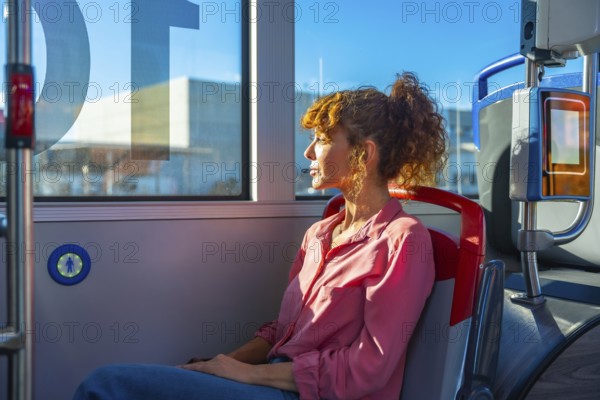Woman seated on a city bus, gazing out the window in quiet thought during commute as sunlight highlights her curly hair and contemplative profile in the urban interior