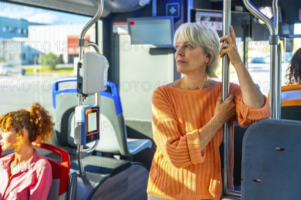 Senior woman standing on a public transport bus, holding a pole and looking out the window, enjoying her daily commute, a young woman seating in the foreground