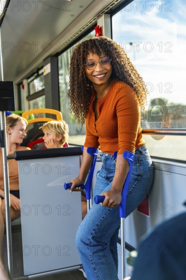 Smiling young woman with crutches standing in a public city bus, commuting happily while other passengers are sitting in the background, showing independence and accessibility