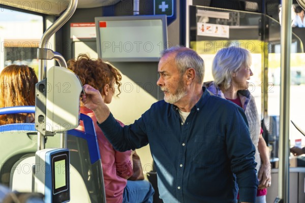 Senior man tapping a contactless fare card on a validator aboard a city bus, surrounded by fellow passengers during a daily commute in urban public transit