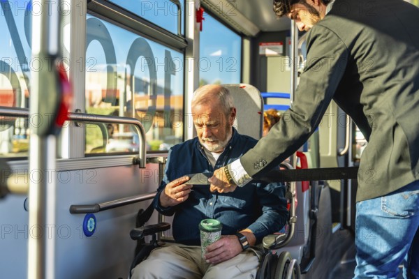 Younger man assisting a senior man in a wheelchair by securing his safety belt, ensuring accessibility, mobility, and safety for passengers on a public transport bus