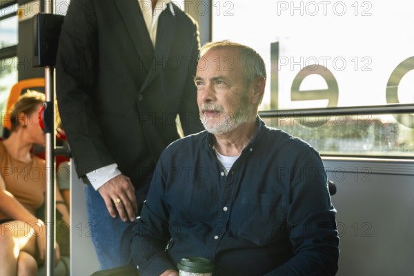 Senior man on a city bus, seated by the window with a reusable cup, gazing thoughtfully outside during a calm urban commute in daylight, relaxed and contemplative