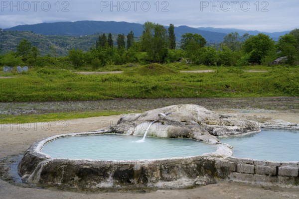 Hot spring pool surrounded by green landscape and forested mountains in the background, springs of Amaghleba, Dikhashkho Sulfur Geyser, hot sulfur springs of Wani, Vani, Imereti region, Georgia