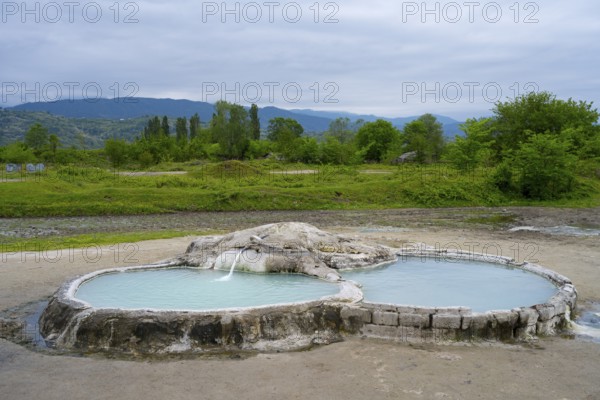 Hot spring pool in open landscape with wooded hills and mountains in the background, springs of Amaghleba, Dikhashkho Sulfur Geyser, hot sulfur springs of Wani, Vani, Imereti region, Georgia