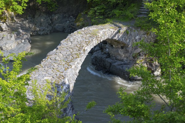 An old stone bridge spans a river amid green trees and rocks, Purtio stone arch bridge, Adjaristskali river, Adjara, Adjaria, Lesser Caucasus, Georgia