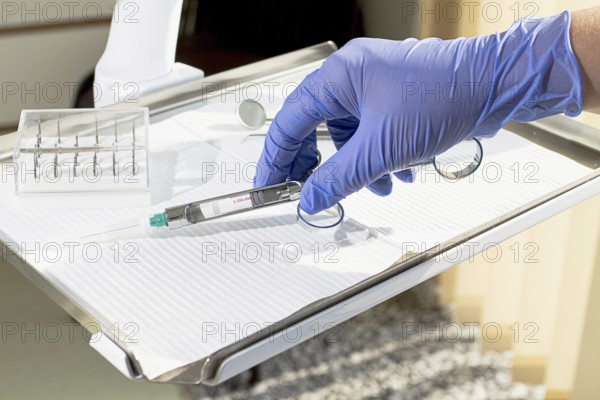 The dentist's hand, in a blue glove, holds a carpal syringe on a tray, ready for a medical procedure