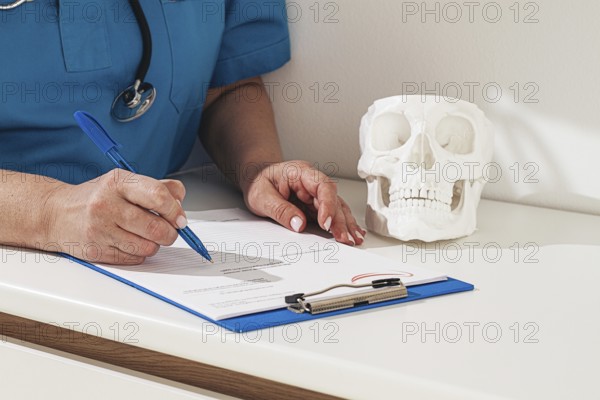 A medical professional reviews the patient's documentation, making notes. There is a model of a skull nearby