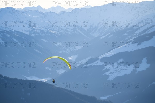 Paragliders flying over snowy mountain peaks in winter in evening light, Kitzbühel Alps, Tyrol, Austria