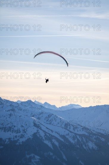 Paragliders flying over snowy mountain peaks in winter in evening light, Kitzbühel Alps, Tyrol, Austria