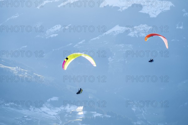 Two paragliders flying in front of snowy mountains in the evening light in winter, Kitzbühel Alps, Tyrol, Austria