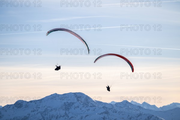 Two paragliders flying in front of snowy mountain peaks in the evening light in winter, Kitzbühel Alps, Tyrol, Austria