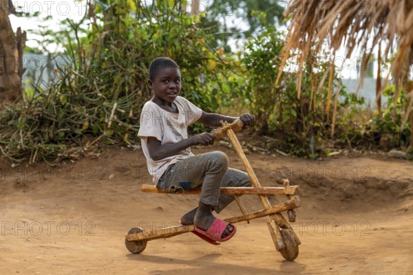 Child on a wooden scooter, homemade toy, in a traditional village, Sadaani, Tanzania