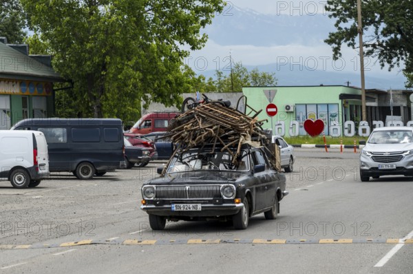Old car with a load of scrap on the roof is driving on a country road, Imereti region, Imereti, Georgia