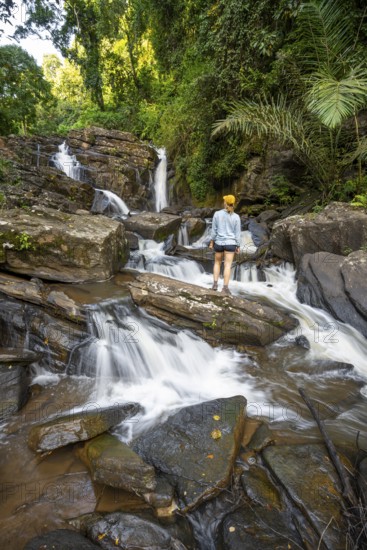 Tourist at Derema Waterfall, flows through dense vegetation, tropical rainforest in Amani Nature Forest Reserve, long exposure, Eastern Usambara Mountains, Tanga, Tanzania