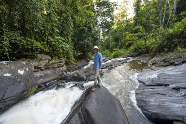Tourist at Derema Waterfall flows through dense vegetation, tropical rainforest in Amani Nature Forest Reserve, long exposure, Eastern Usambara Mountains, Tanga, Tanzania