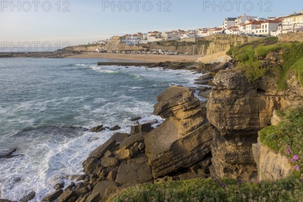 Coastal town with rocky cliffs by the sea and calm water at sunset, coast near Ericeira, Portugal