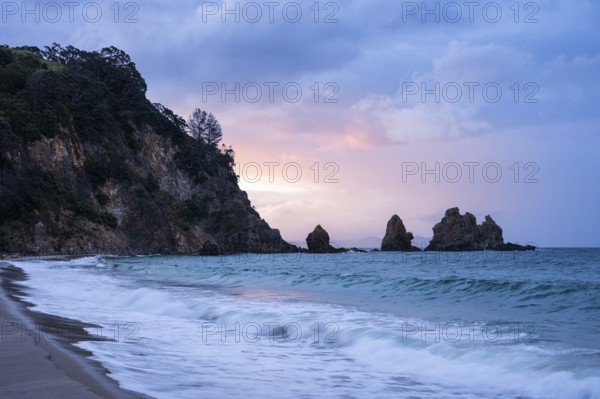 Landscape with sea, rocks and sandy beach in New Zealand in the evening at sunset. Otama Beach, Coromandel Peninsula, Waikato, New Zealand