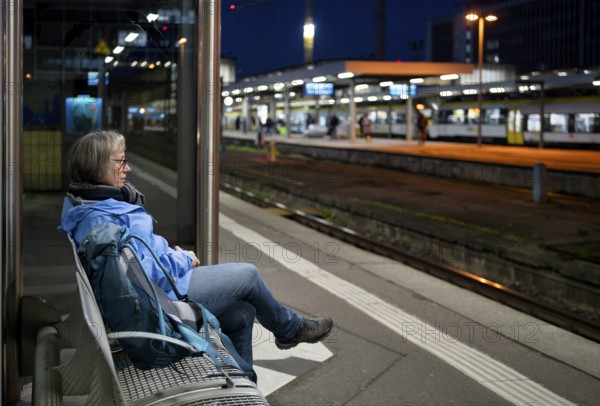 Night shot, elderly woman, traveler, sitting alone on a bench at the platform, backpack, main train station, Stuttgart, Baden-Württemberg, Germany