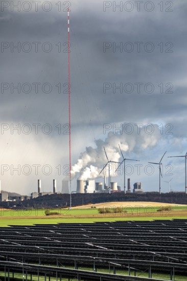 86.5 MW peak open space photovoltaic systems, from RWE, with over 141, 000 solar modules, on a side strip, along the A44 motorway near Jüchen, at the timber triangle, recultivated open-cast mining area, in the background RWE brown coal power plant Neurath, wind farm, world highest wind measurement tower, 300m to research wind potential in the region, North Rhine-Westphalia, Germany