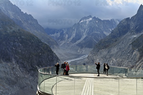 A group of people take pictures of themselves on the viewing platform in front of the Mer de Glace glacier, Mont-Blanc, Chamonix-Mont-Blanc, Haute-Savoie, France