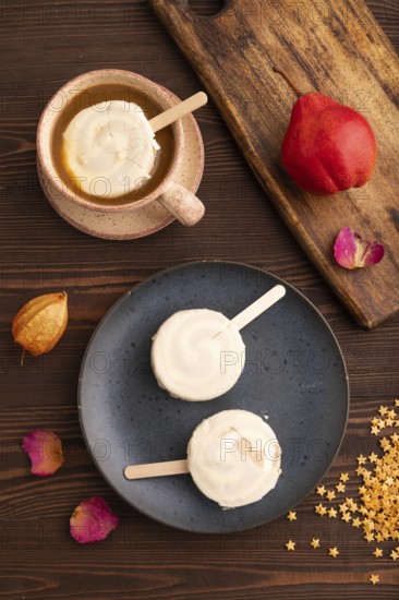 ?hocolate Ice cream in white glaze, cup of coffee, on brown wooden background, top view, flat lay, close up