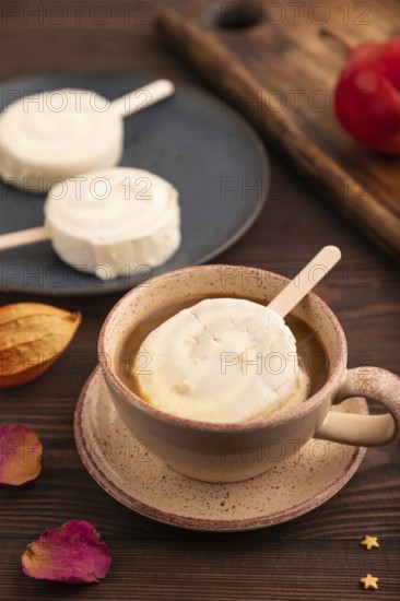 ?hocolate Ice cream in white glaze, cup of coffee, on brown wooden background, side view, close up, selective focus