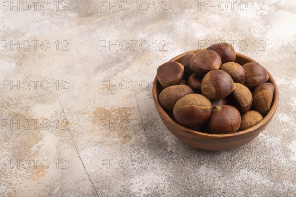 Wooden bowl with raw edible ?hestnuts on brown concrete background, side view, copy space, minimalism