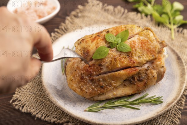 Fried Turkey Thigh with spices and rosemary on plate with hand on brown wooden background and linen textile. side view, close up, selective focus