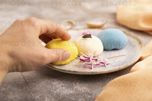 Japanese Mochi Cakes with hand on brown concrete background and orange textile, side view, close up, selective focus