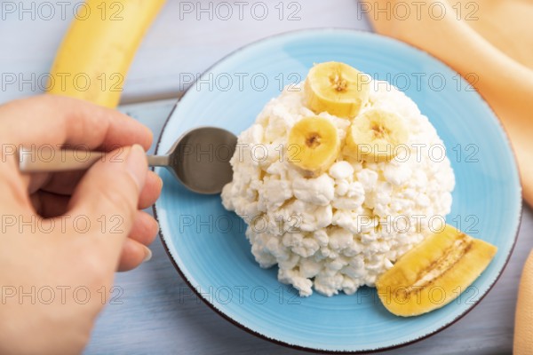 White ?ottage cheese, Curd, with Banana with hand on blue wooden background and orange textile, side view, close up, selective focus
