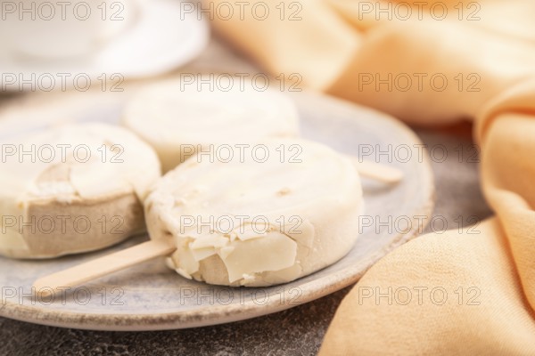?hocolate Ice cream in white glaze, cup of coffee, on brown concrete background and orange textile, side view, close up, selective focus, minimalism