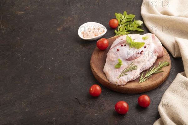 Raw Turkey Thigh with spices and rosemary on cutting board on black concrete background and linen textile. side view, copy space