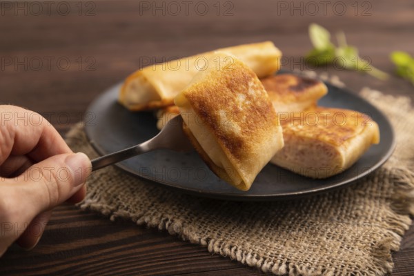 Fried crispy pancakes with meat and cheese with hand on brown wooden background and linen textile. side view, close up, selective focus