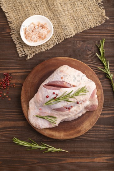 Raw Turkey Thigh with spices and rosemary on cutting board on brown wooden background and linen textile. top view, flat lay, close up