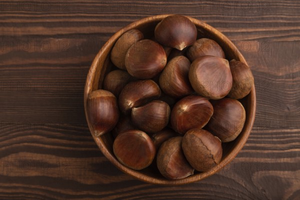 Wooden bowl with raw edible ?hestnuts on brown wooden background, top view, flat lay, close up, minimalism